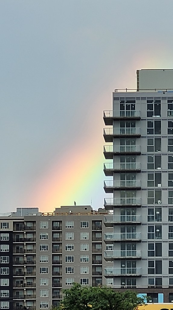 A chunky rainbow peaking through behind an L shaped condo building.
